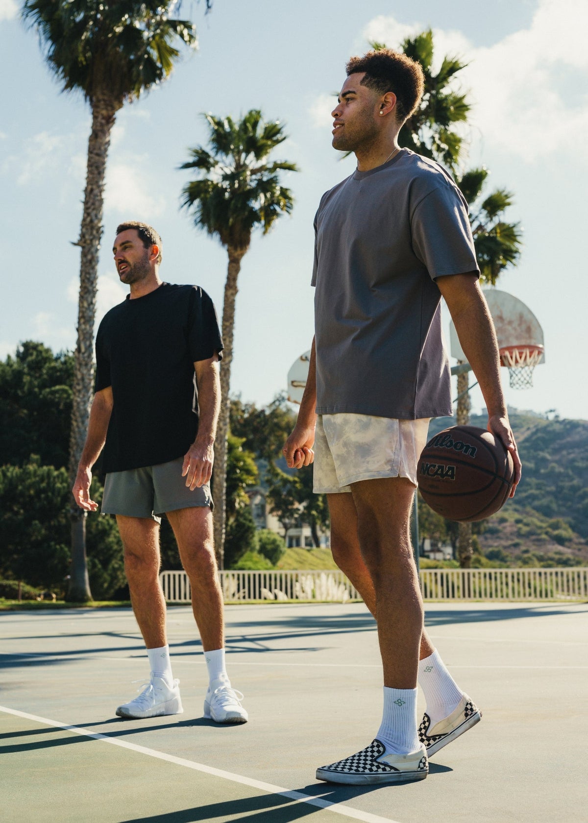 Two men on a basketball court with palm trees in the background